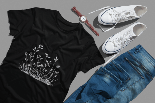 Flat lay of a black Dudle t-shirt with white floral doodle design, jeans, sneakers, and a wristwatch